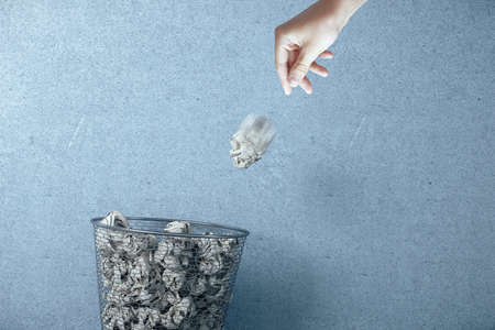 Hand trowing a paper into a wastebasket on blue background. Business and paperwork concept.の写真素材