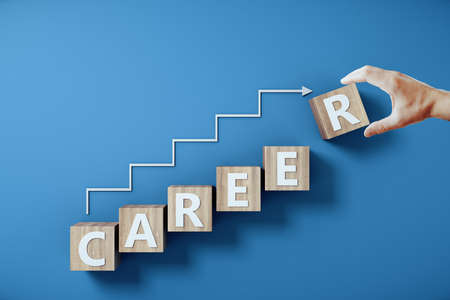 Hand holding career word on wooden cubes with arrow in form staircase on blue background. Success and career ladder concept.の写真素材
