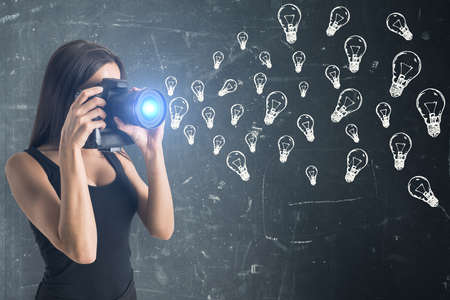 Young woman shoots on camera with drawing lamps sketch on blackboard. Brainstorm and innovation conceptの写真素材
