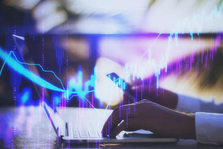 Businessman hands using phone and laptop with stock chart and statistic hologram. Business and...