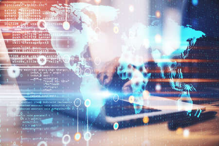 Hand using laptop on desktop with world map hologram on creative glowing programming backdrop....