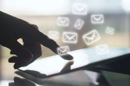 Side view of female hand using tablet with digital email icon on blurry background. E-mail marketing...
