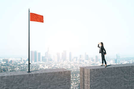 Businesswoman standing on concrete block and looking on red flag on city background. Success and...