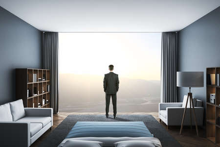Businessman standing in clean living room with panoramic city view and two sofa. Occupation and worker concept.の写真素材
