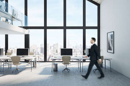 Businessman walking in coworking two-story loft office interior with computers on table and city view. Occupation and worker concept.の写真素材