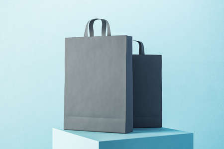 Two black paper shopping bag with handles on blue podium. Trade and gift concept. 3D Renderingの写真素材