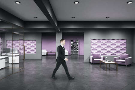 Businessman walking in coworking office room with computers and shelf with books. Workplace and...