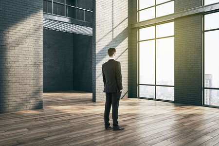 Businessman standing in gallery interior with big windows. Performance and presentation concept. Mock upの写真素材