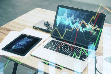 Top view laptop with stock chart on screen, supplies and other items on wooden table. Mock up, 3D...