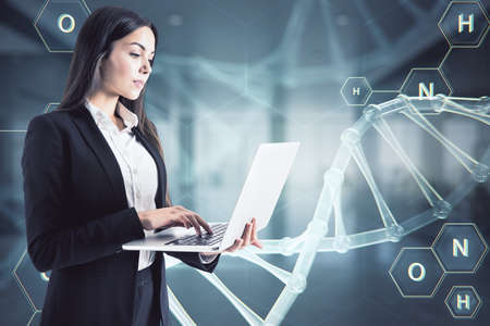 Woman working with laptop on a virtual DNA hologram backgroundの写真素材
