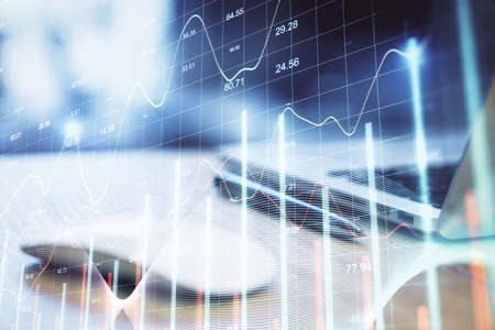 Computer mouse and laptop on table with stock charts hologram. Trade and financial growth concept....