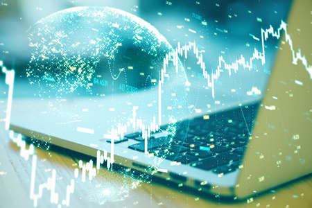 Laptop on table with stock charts and earth hologram. Trade and financial growth concept. Close up
