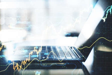 Laptop computer on desktop with stock charts interface. Trade and financial growth concept. Close up