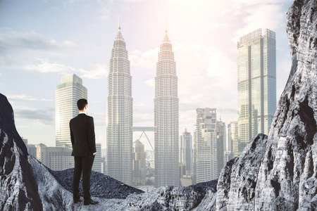 New heights concept with businessman on the rock looking at city skyscrapers in smoke. Double...