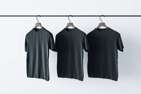 Make a sign concept with three blank black t-shirts hanging on a rail at white background. Mockup. 3D renderingの写真素材