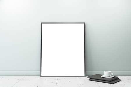 White blank poster in black frame on marble floor near black books with cup of coffee leaning on...