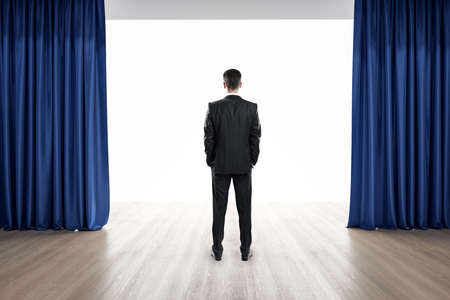 Oratory concept with businessman preparing to speak staying on wooden floor between blue curtainsの写真素材