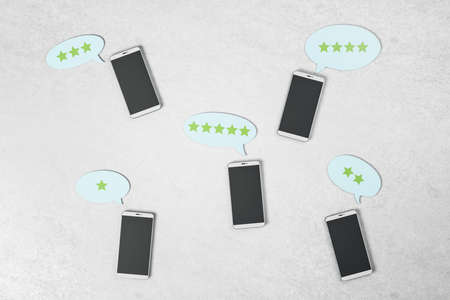 Rating feedback review concept with black smartphone screens on light concrete surface and stars in...