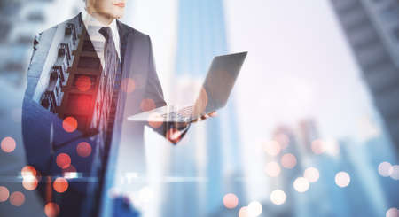 Remote working concept with employer in black suit with opened laptop at blurry city skyscrapers...