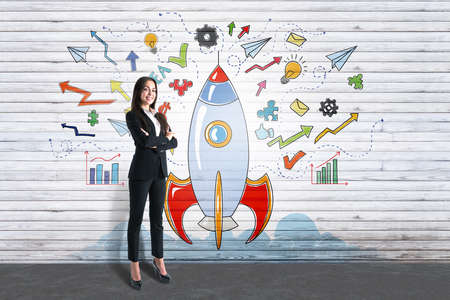 Start up and business idea concept with satisfied businesswoman on light brick wall with handwritten colorful rocket sketch backgroundの写真素材