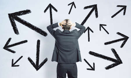 Difficult decision concept with man in black suit grabs his head in front of white wall with black...