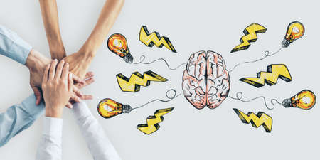 Brainstorming concept with business people hands on white surface and handwritten brain parts, light bulbs and lightning symbolsの写真素材