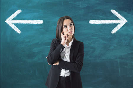 Make the choice concept with pensive businesswoman on green chalkboard with white arrows backgroundの写真素材