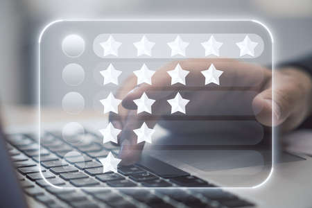 Giving customer feedback concept with digital display with star ratings on man hand typing on laptop keyboard backgroundの写真素材