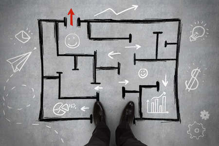 Feet standing in the beginning of a black drawn sketch on a concrete floor background with multiple white icons, pathway and challenge conceptの写真素材