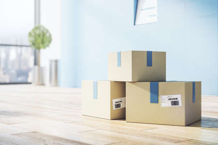 Delivery service concept with cardboxes with barcodes on wooden floor in empty sunny room with blue...