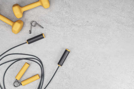 Online sport training concept with yellow dumbbells and black skipping rope on abstract concrete background with copyspace. 3D rendering, mockupの写真素材