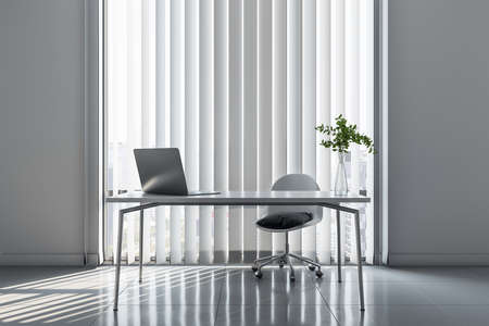 Stylish workplace in minimalistic office room with light table and chair, modern laptop, blinds on windows and sunlight on glossy floor. 3D renderingの写真素材