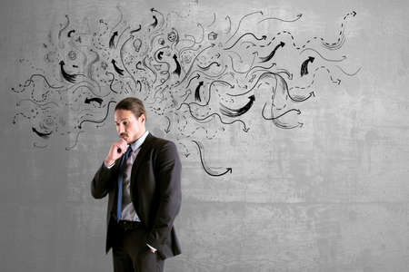 Choice concept with pensive buisnessman on concrete wall background with black arrows directed in different directionsの写真素材