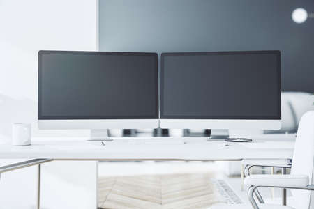 Black computer monitors with copyspace for your text on white table in stylish sunny room with...