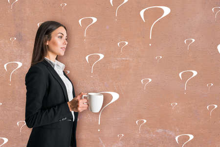 Business support concept with young woman in black jacket with coffee cup on concrete wall background with question marksの写真素材