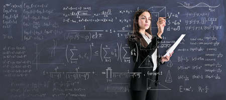 Studying process with young woman in black suit writing on transparent wall math calculationsの写真素材
