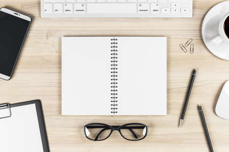Stylish work table with blank notebook pages, keyboard, glasses, smartphone and coffee mug on wooden...