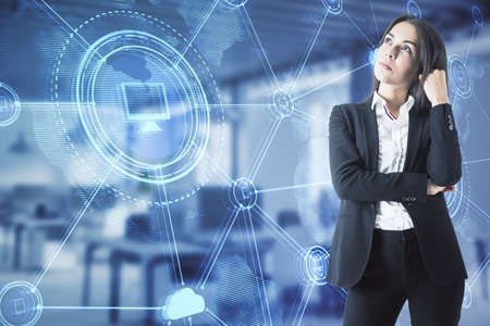 Thoughtful young european businesswoman standing in blurry office interior with abstract glowing digital business interface. Double exposureの写真素材