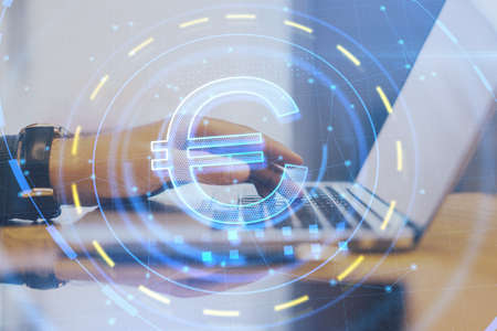 Side view of businessman hands using laptop with glowing euro sign at blurry desktop. Investment, online banking and trade concept. Double exposureの写真素材