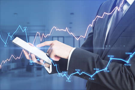 Businessman hands using tablet with abstract glowing forex chart in blurry office interior. Economy,...