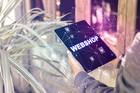 Close up of man hands using tablet with creative webshop inscription on screen. Wooden exterior and...