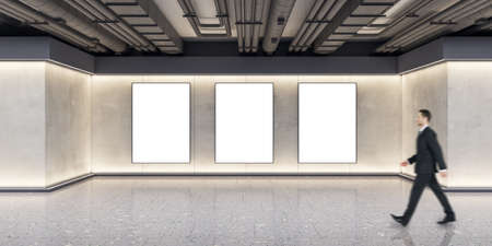 Businessman walking in modern exhibition space concrete interior with empty posters on wall. Mock up