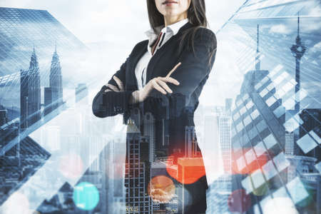Businesswoman with folded arms standing on abstract city backdrop.の写真素材