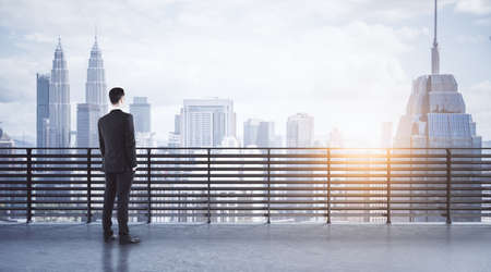 Leader and success concept with businessman on rooftop with slatted fence and megapolis city buildings view at sunsetの写真素材