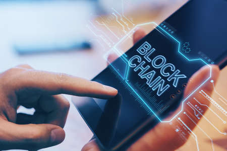 Close up of hand using digital tablet with creative blockchain hologram on blurry wooden office...