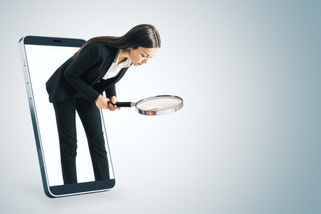 Attractive young european businesswoman inside abstract smartphone with magnifier searching for something on white background with mock up place. Online research conceptの写真素材