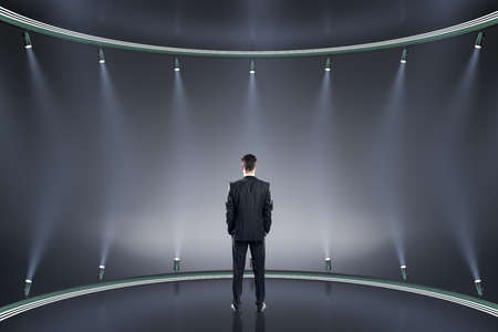 Back view of young businessman on creative stage background with illumination. Spotlight and fame...
