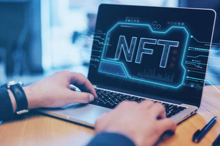 Close up of hands at wooden office desktop using laptop keyboard with glowing NFT chip hologram on blurry background. Non-fungible token and crypto currency concept. Double exposureの写真素材