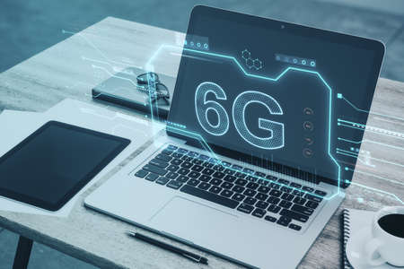 Close up of wooden desktop with laptop and other items, creative 6G chip hologram on blurry...