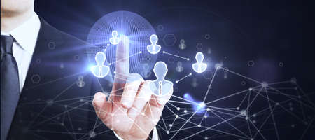 Businessman hand using glowing globe interface with people icons on dark background. Social networking and recruiting conceptの写真素材